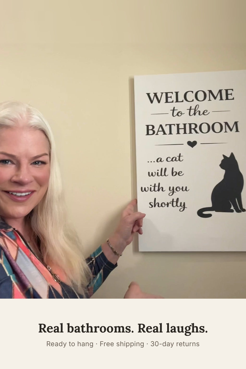 Woman smiling next to the funny cat bathroom canvas hanging on her wall