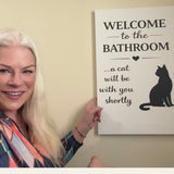 Woman smiling next to the funny cat bathroom canvas hanging on her wall